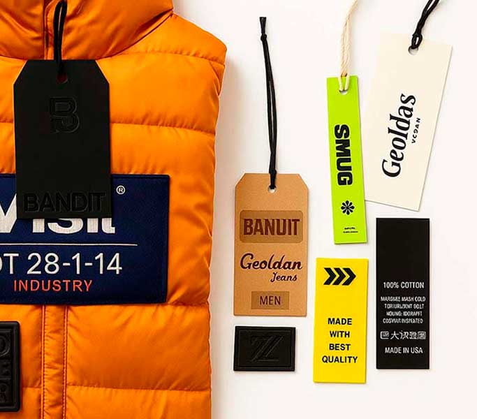 Colección de hang tags de cartón, placas PVC y etiquetas tejidas sobre una chaqueta, fabricados al por mayor en Bogotá con calidad premium para mayoristas.