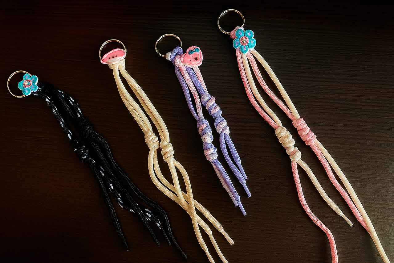 Llaveros y apliques con cordones trenzados de colores sobre fondo oscuro.
