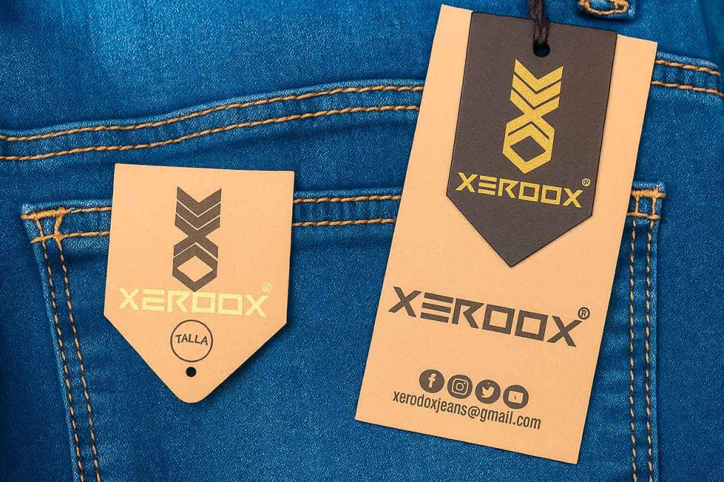 Etiqueta colgante ecológica de cartón reciclado en jeans azules, con logo de marca y diseño moderno.