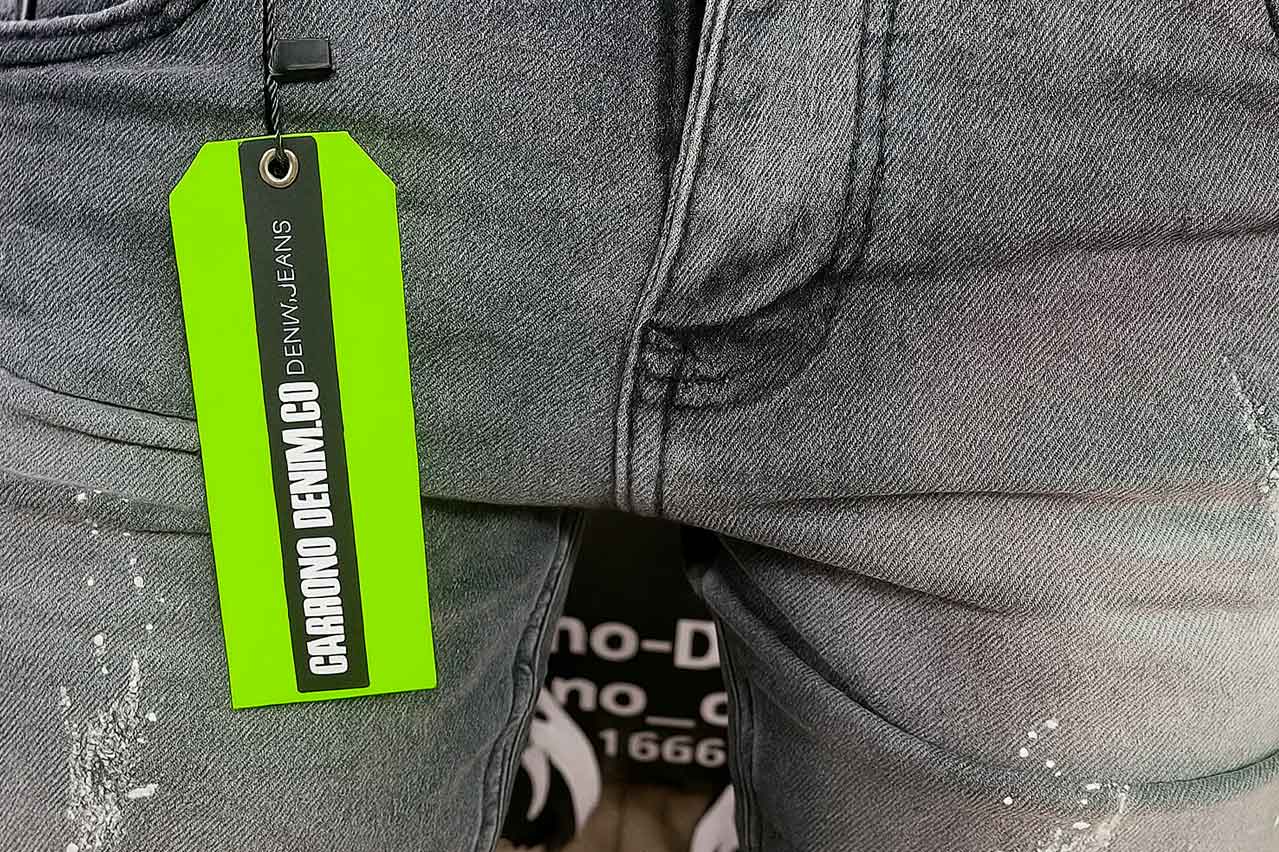 Marquillas y etiquetas de cartón colgante de cartón color neón con cinta negra, atada a un jean gris desgastado.