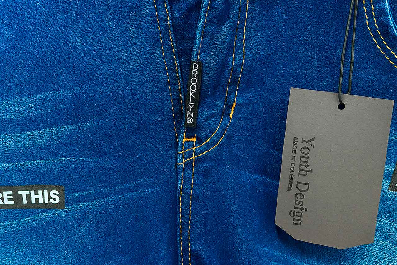 Etiqueta colgante en cartón color gris con cordón, personalizada con la marca Youth Design, colgada en un pantalón jean azul.