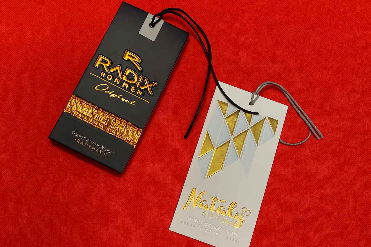 Etiquetas dobles en cartón con detalles en alto relieve y acabado brillante para prendas de alta gama.