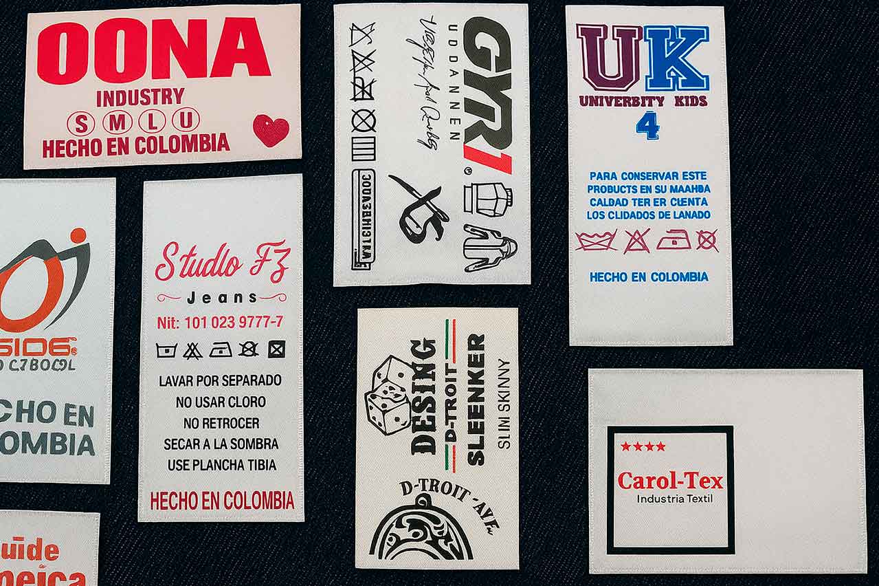 Fabricación de etiquetas estampadas satín con instrucciones de lavado impresas, variedad de diseños sobre fondo textil oscuro.