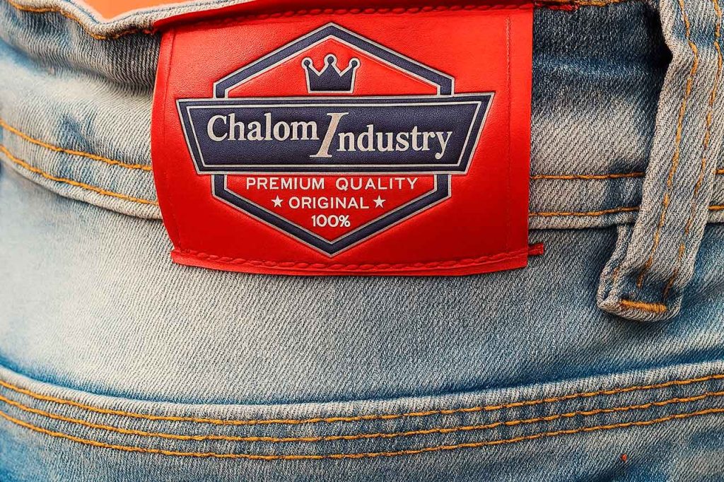 Etiqueta tipo garra en cuero sintético rojo con impresión screen para jeans. Diseño plano, colores definidos y acabado profesional.