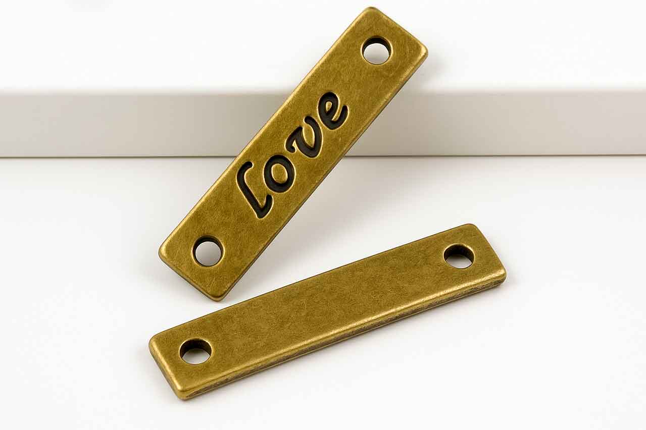 en marcatex tenemos fabricación de placas metalicas para ropa con la palabra Love, fabricada en Zamak, con acabado envejecido y perforaciones para costura. Ideal para camisas elegantes.